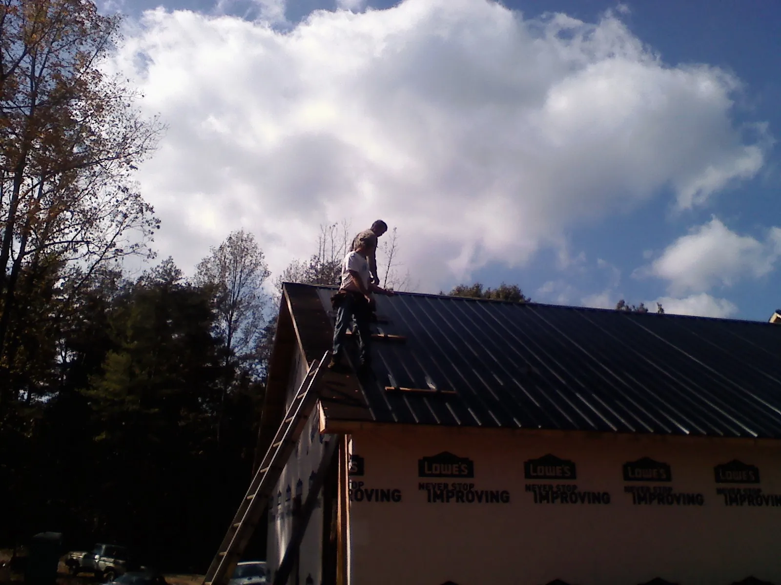 Roofer fastening dark metal panels high against a cloudy sky, from a Roof Inspection job in Frazier Park