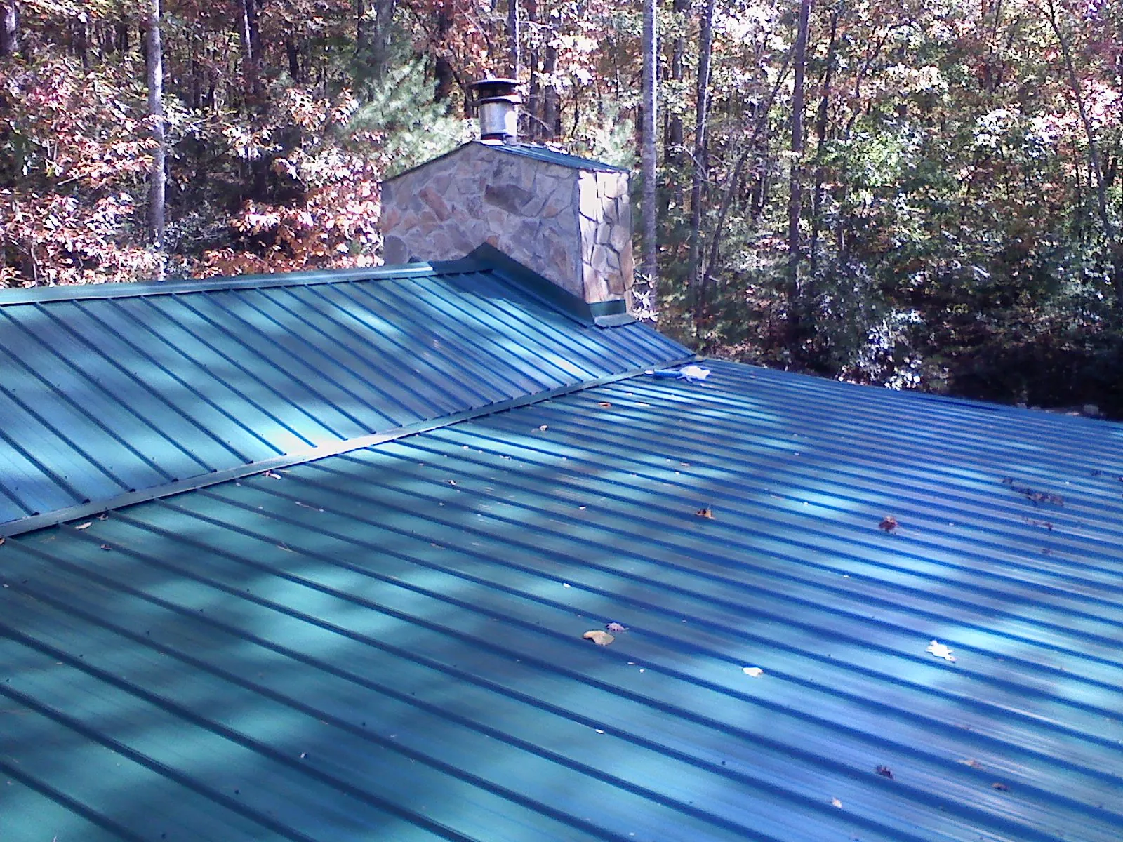 New green metal roof and stone chimney surrounded by autumn woods in Frazier Park