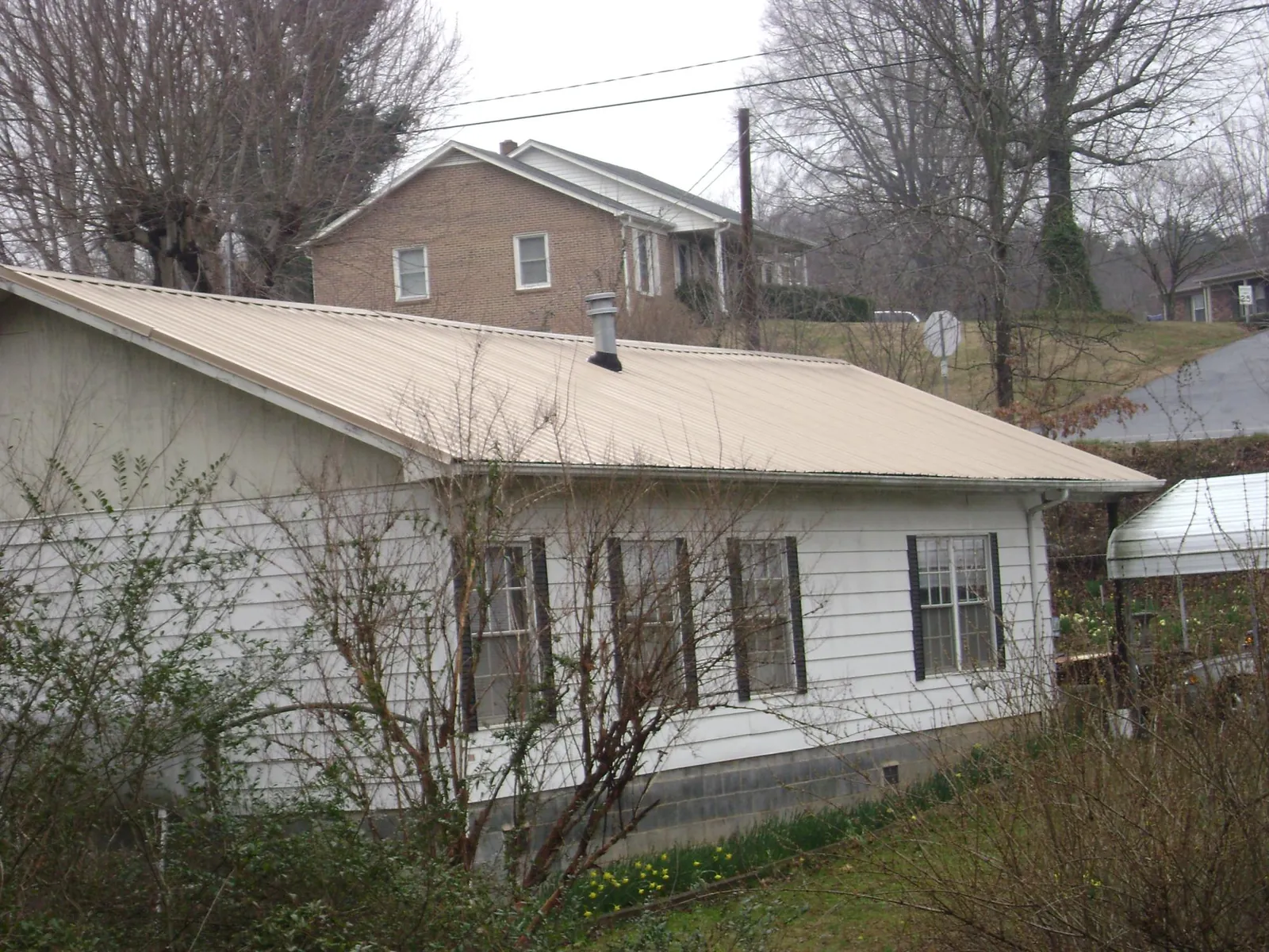 Tan metal roof on a white sided house set into a hillside — Commercial Roofing by Roofing Brothers in Frazier Park